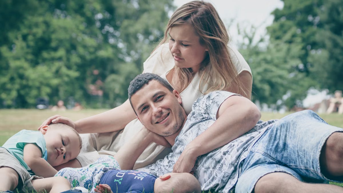Happy family enjoying a sunny day outdoors, with parents and children lying on the grass.